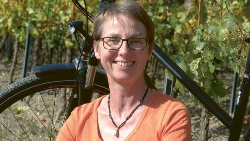 Portrait: Autorin Annette Sievers vor ihrem Fahrrad mit Weinreben im Hintergrund