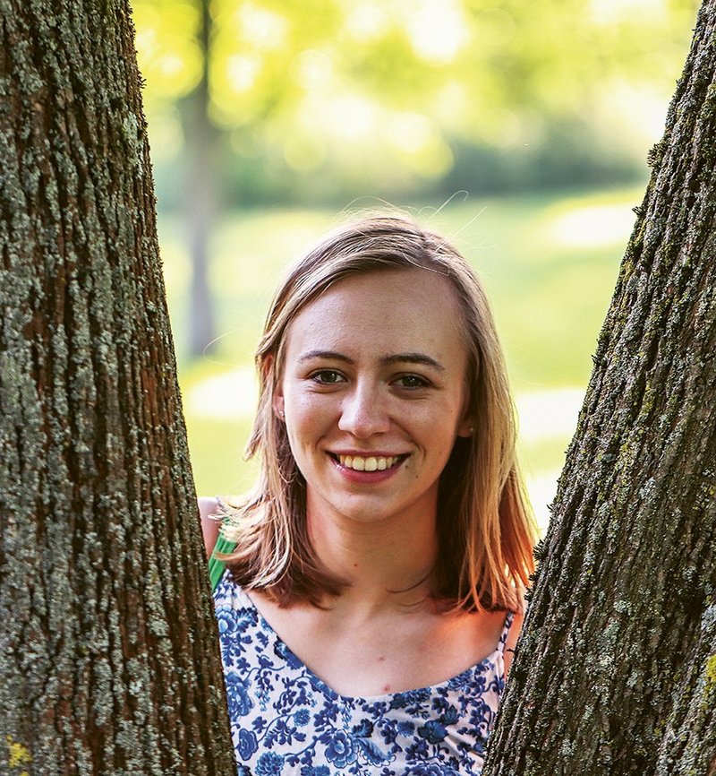 Portrait: Autorin Hannah Mehrfert zwischen zwei Baumstämmen