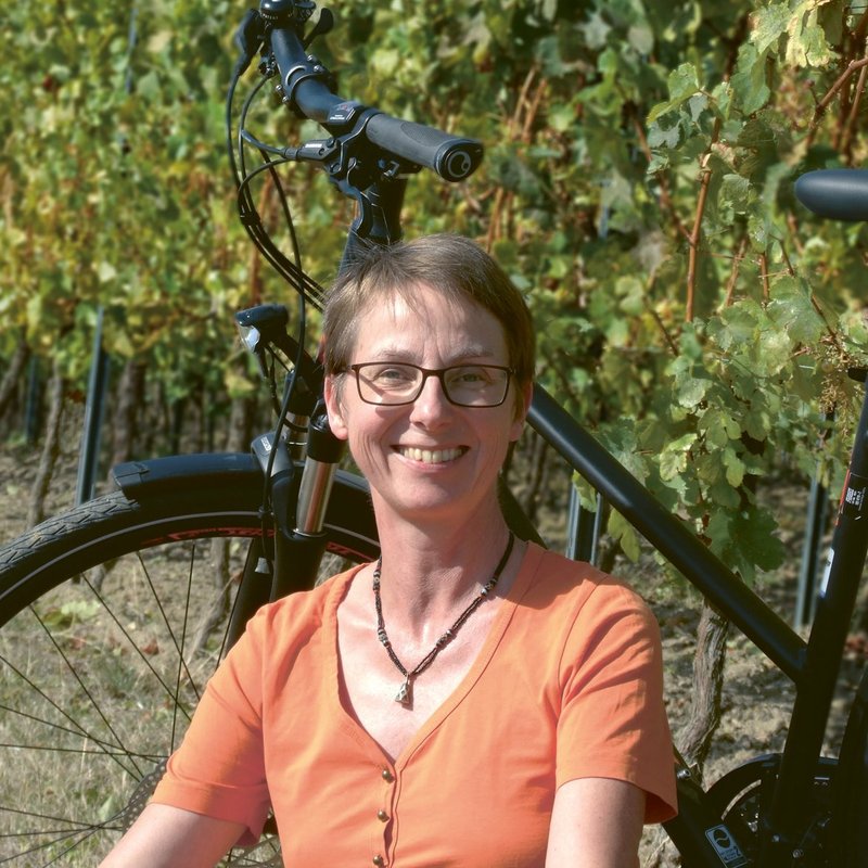 Portrait: Autorin Annette Sievers vor ihrem Fahrrad mit Weinreben im Hintergrund