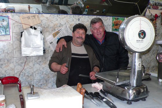 Zwei Freundestehen hinter der Metzgertheke und halten sich im Arm. Sie lachen in die Kamera