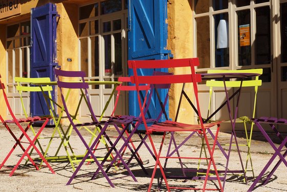 Bunte Klappstühle vor einem blauen Türladen, Abendstimmung in der Provence