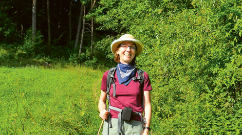 Autorin Annette Sievers wandert mit Stock in der Hand durch Wiesen am Waldrand entlang