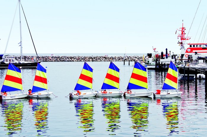 Kleine Segelboote mit bunten Segeln schippern in der Gruppe entlang der Ostseeküste