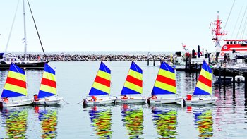 Kleine Segelboote mit bunten Segeln schippern in der Gruppe entlang der Ostseeküste